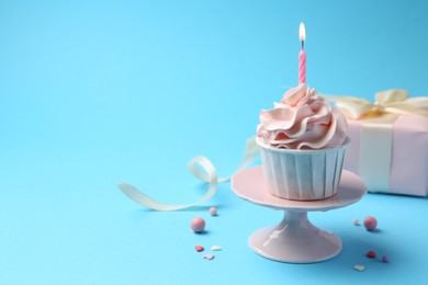 Photo of Delicious birthday cupcake with burning candle and sprinkles on light blue background, closeup. Space for text