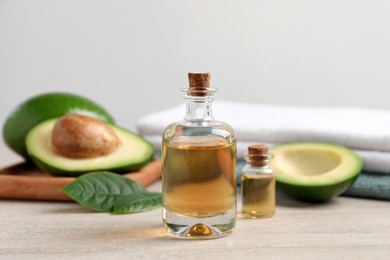 Bottles of essential oil, fresh avocado and towels on light wooden table