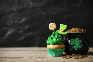 Decorated cupcake and pot with gold coins on wooden table, space for text. St. Patrick's Day celebration