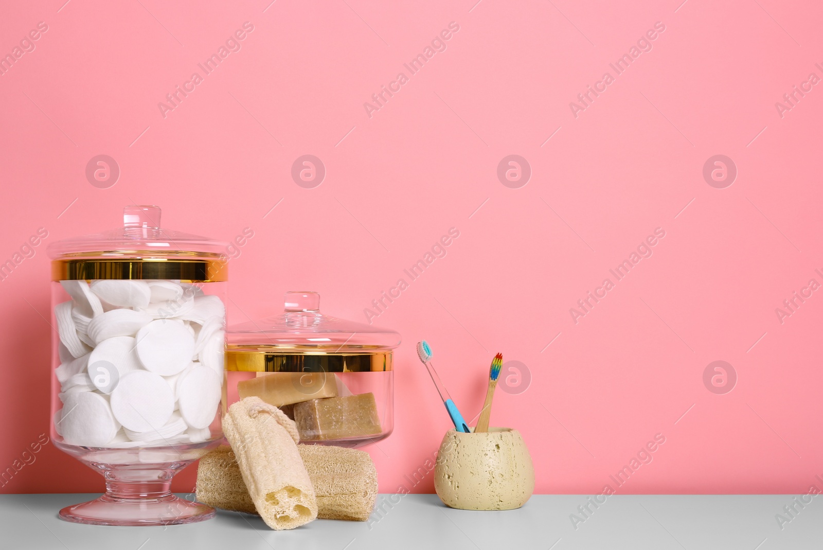 Photo of Composition of glass jar with cotton pads on table near pink wall. Space for text