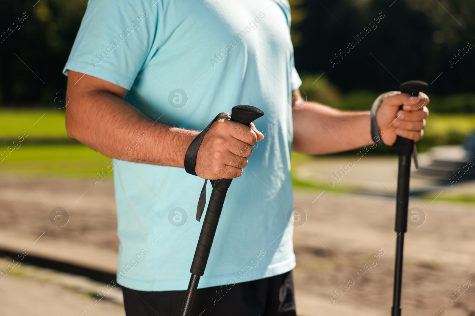 Photo of Man practicing Nordic walking with poles outdoors on sunny day, closeup