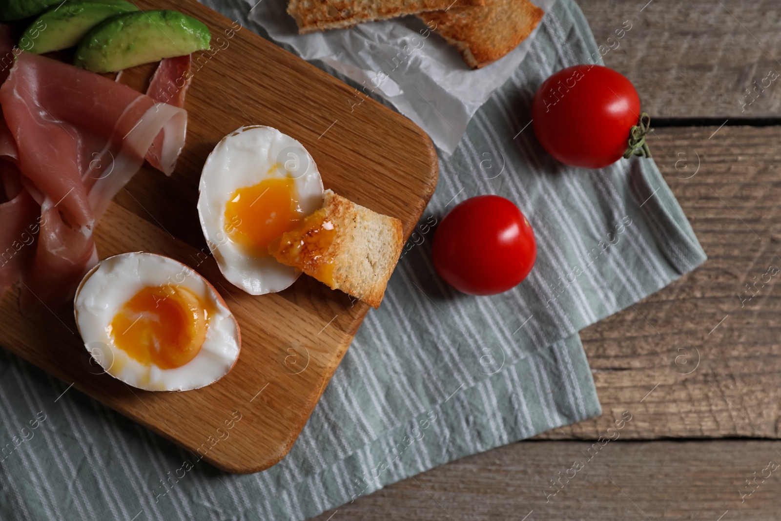 Photo of Delicious breakfast with soft boiled egg and tasty prosciutto served on wooden table, flat lay