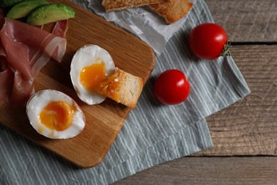 Delicious breakfast with soft boiled egg and tasty prosciutto served on wooden table, flat lay