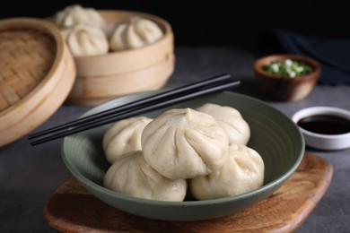 Photo of Delicious bao buns (baozi) in bowl and chopsticks on grey table, closeup
