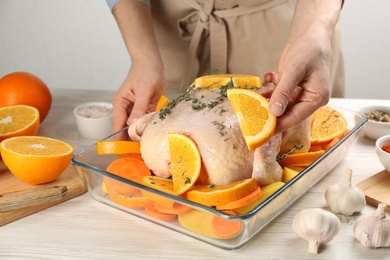 Woman adding orange slice to raw chicken at white wooden table, closeup