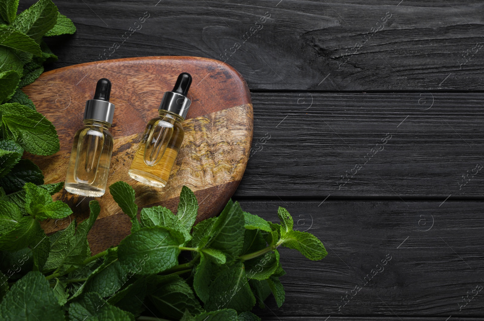 Photo of Bottles of mint essential oil and green leaves on black wooden table, flat lay. Space for text