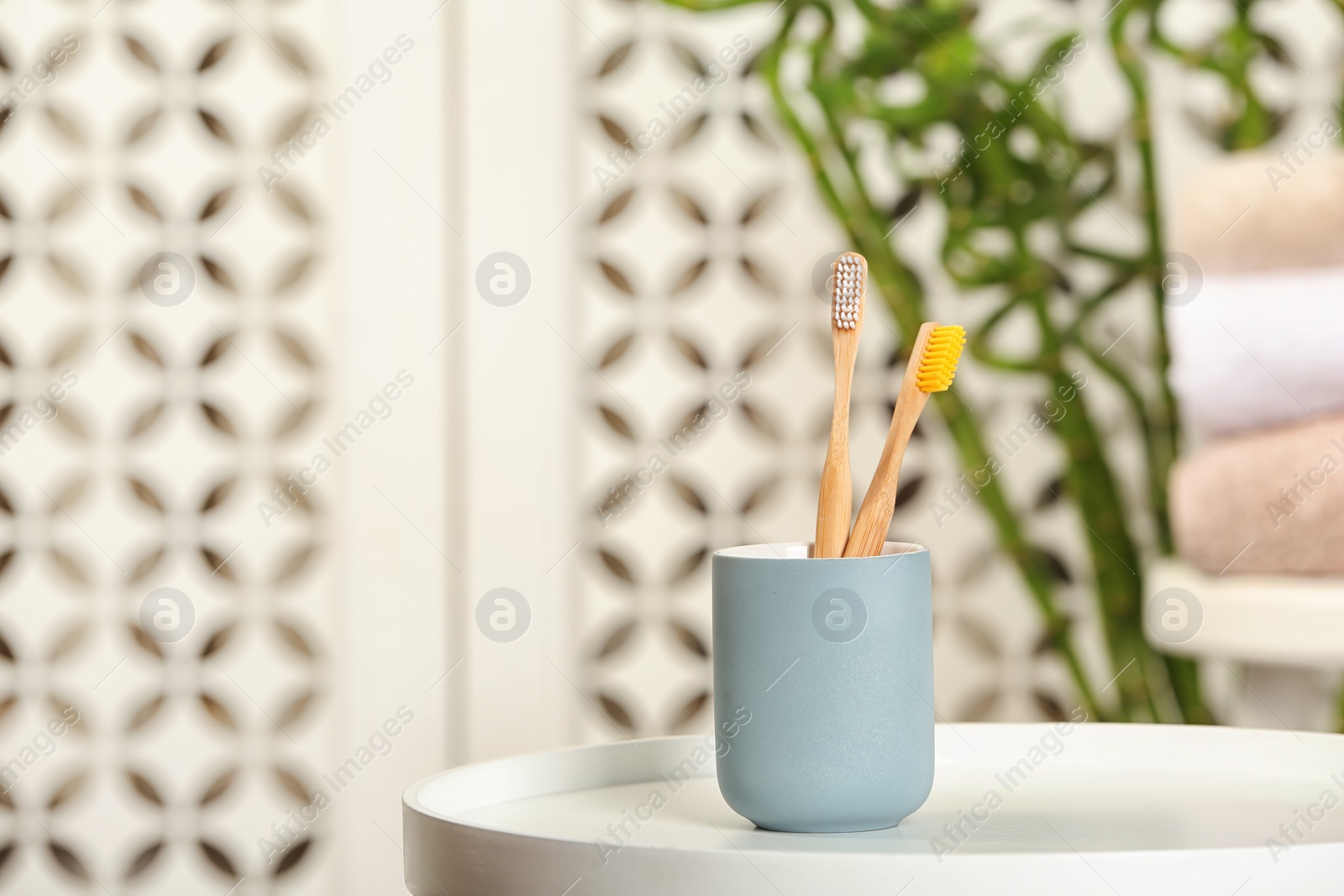 Photo of Holder with bamboo toothbrushes on table against blurred background