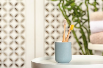 Photo of Holder with bamboo toothbrushes on table against blurred background