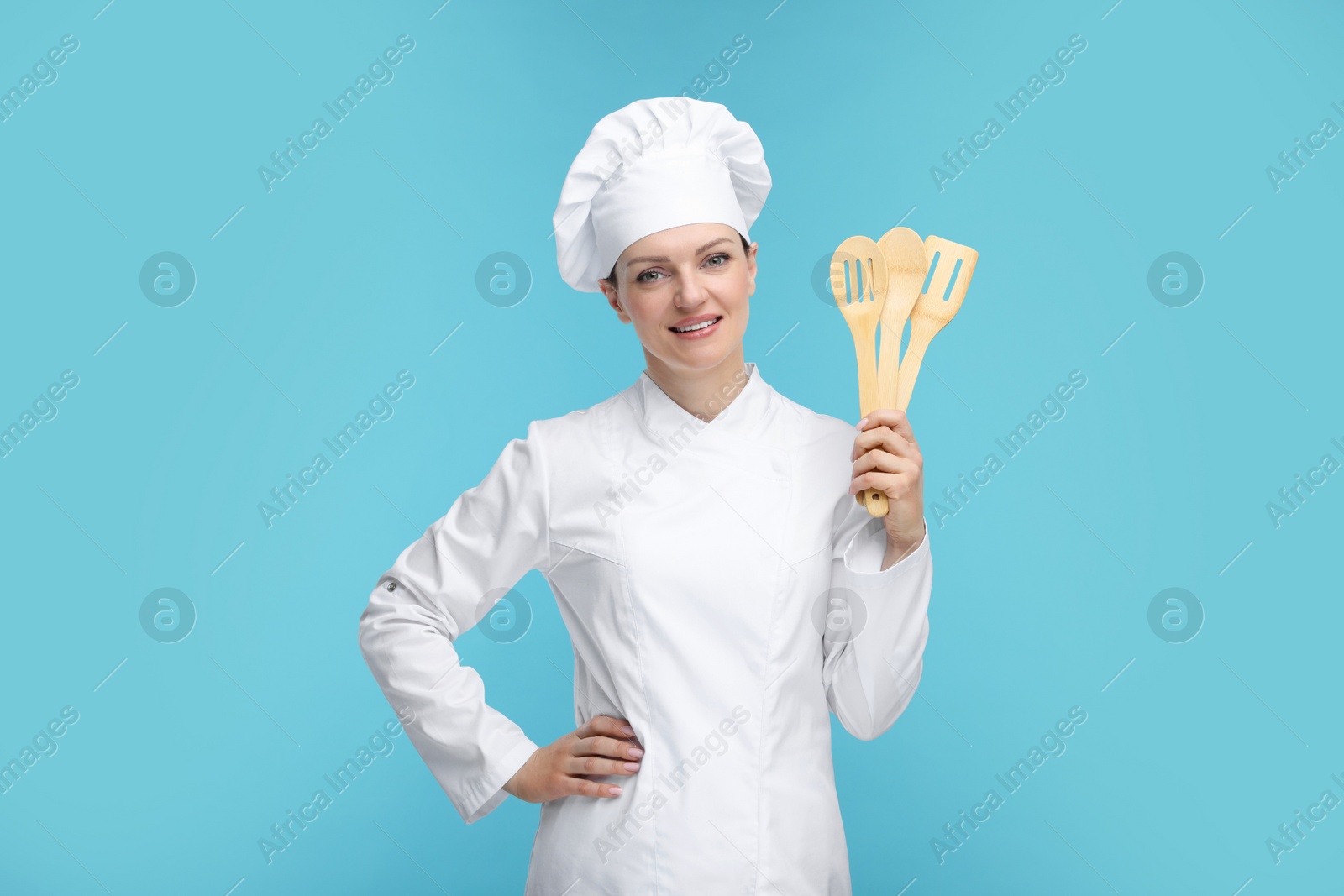 Photo of Happy chef in uniform holding wooden utensils on light blue background