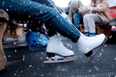 Image of Young woman wearing white ice skates on bench outdoors, closeup