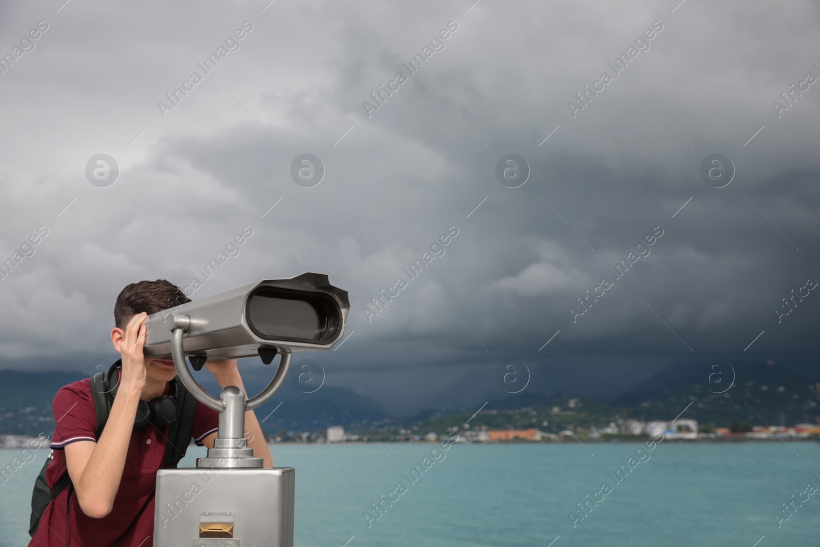 Photo of Teenage boy looking through mounted binoculars near sea. Space for text