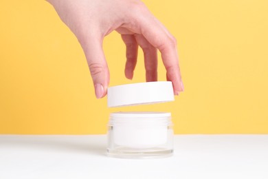 Photo of Woman with jar of cream on yellow background, closeup