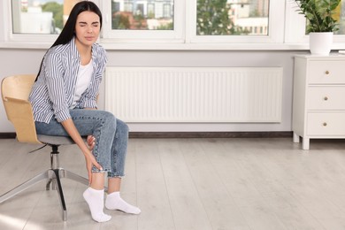 Woman suffering from leg pain on chair at home, space for text