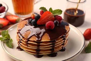 Stack of tasty pancakes with fresh berries, chocolate sauce and mint on white table, closeup