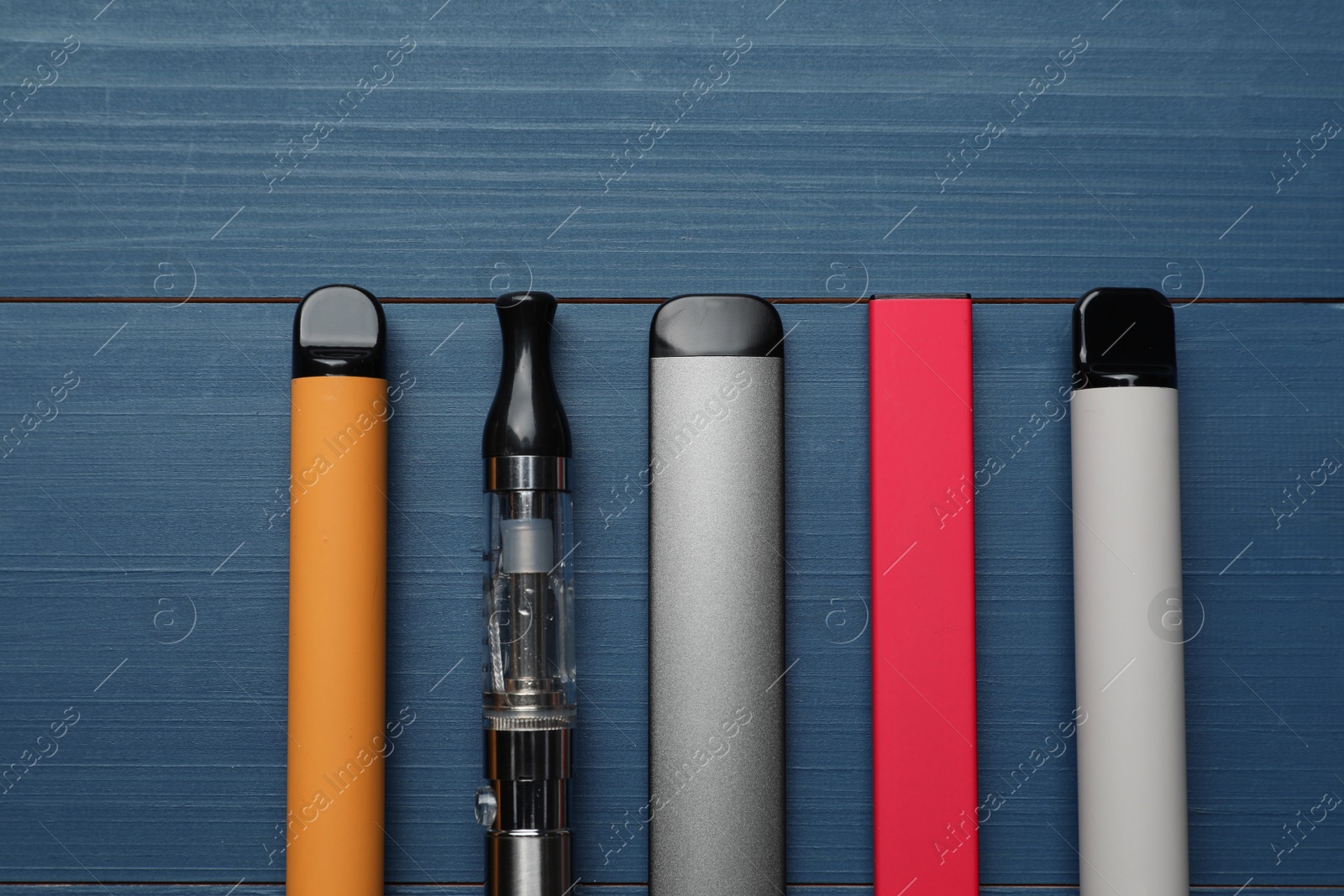 Photo of Different electronic cigarettes on blue wooden background, flat lay