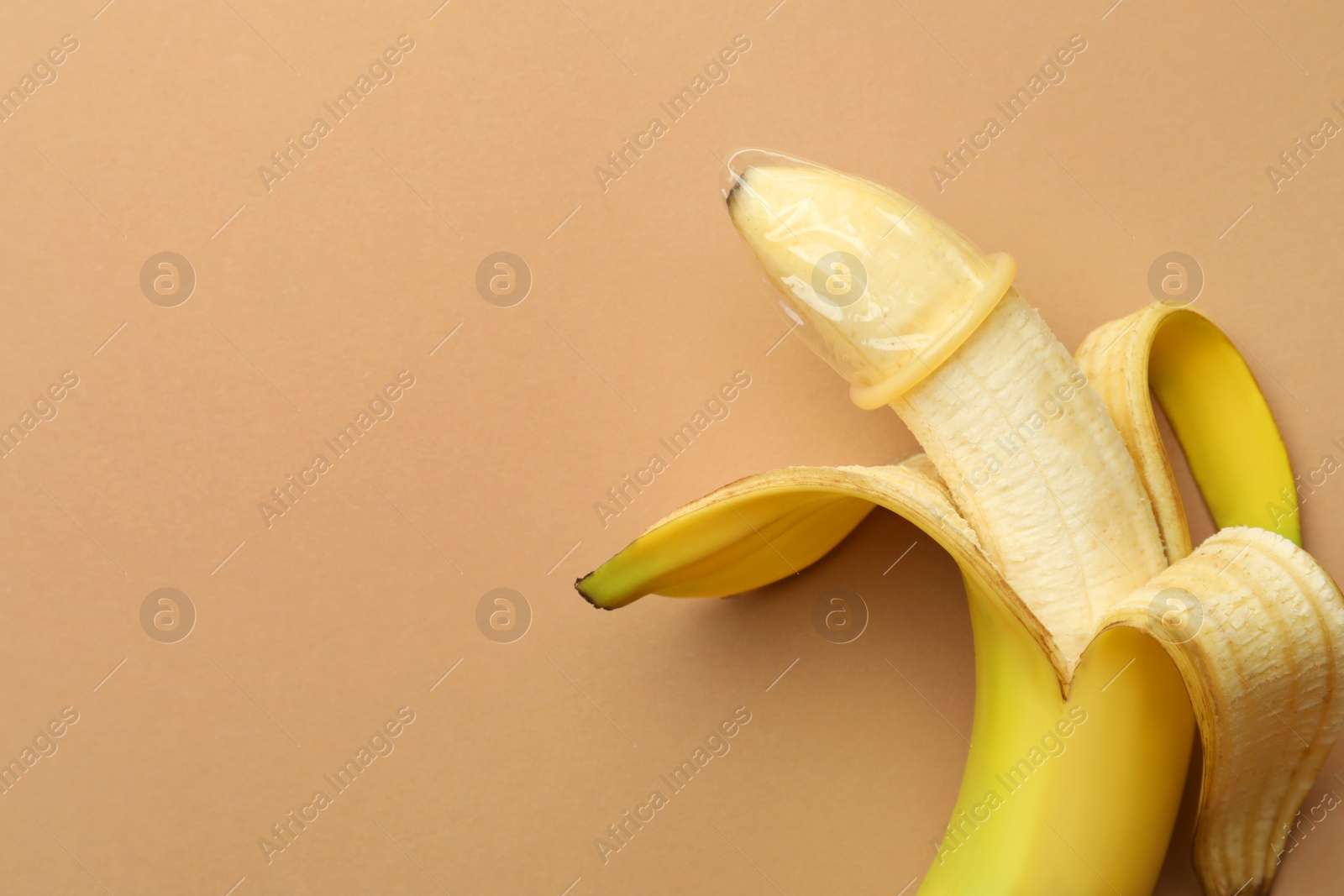 Photo of Banana with condom on pale orange background, top view and space for text. Safe sex concept