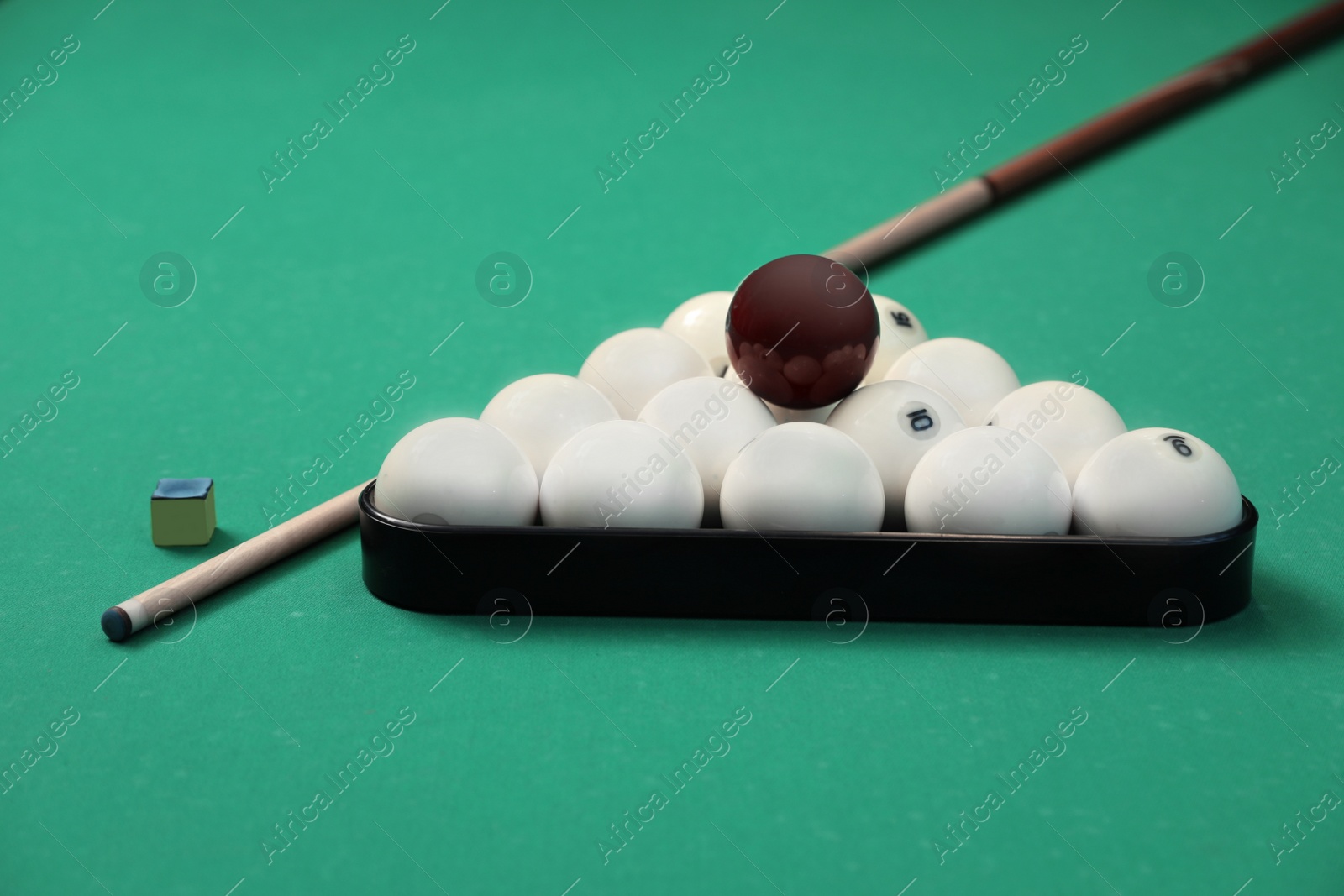 Photo of Billiard balls in triangle rack, cue and chalk on table