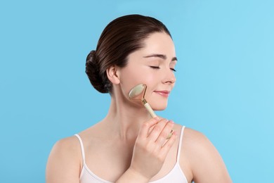Young woman massaging her face with jade roller on turquoise background