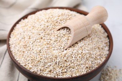 Photo of Dry barley groats and scoop in bowl on white table, closeup