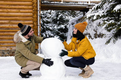 Photo of Happy couple making snowman together outdoors. Winter vacation
