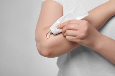 Photo of Woman applying ointment from tube onto her arm on light grey background, closeup