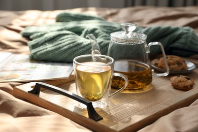 Wooden tray with freshly brewed tea and cookies on bed in room. Cozy home atmosphere