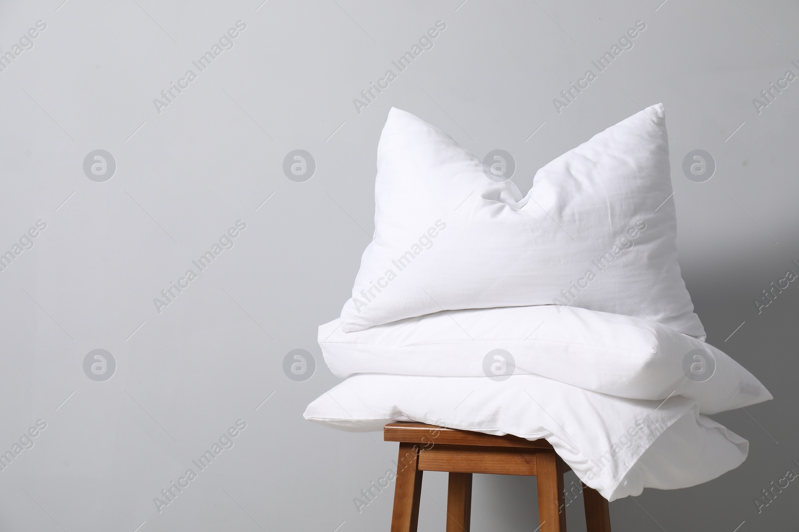 Photo of Soft pillows on chair neal light grey wall, space for text