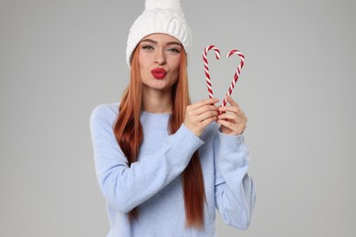 Young woman in hat and sweater with candy canes on light grey background. Christmas celebration