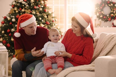 Photo of Happy couple with cute baby on sofa in room decorated for Christmas