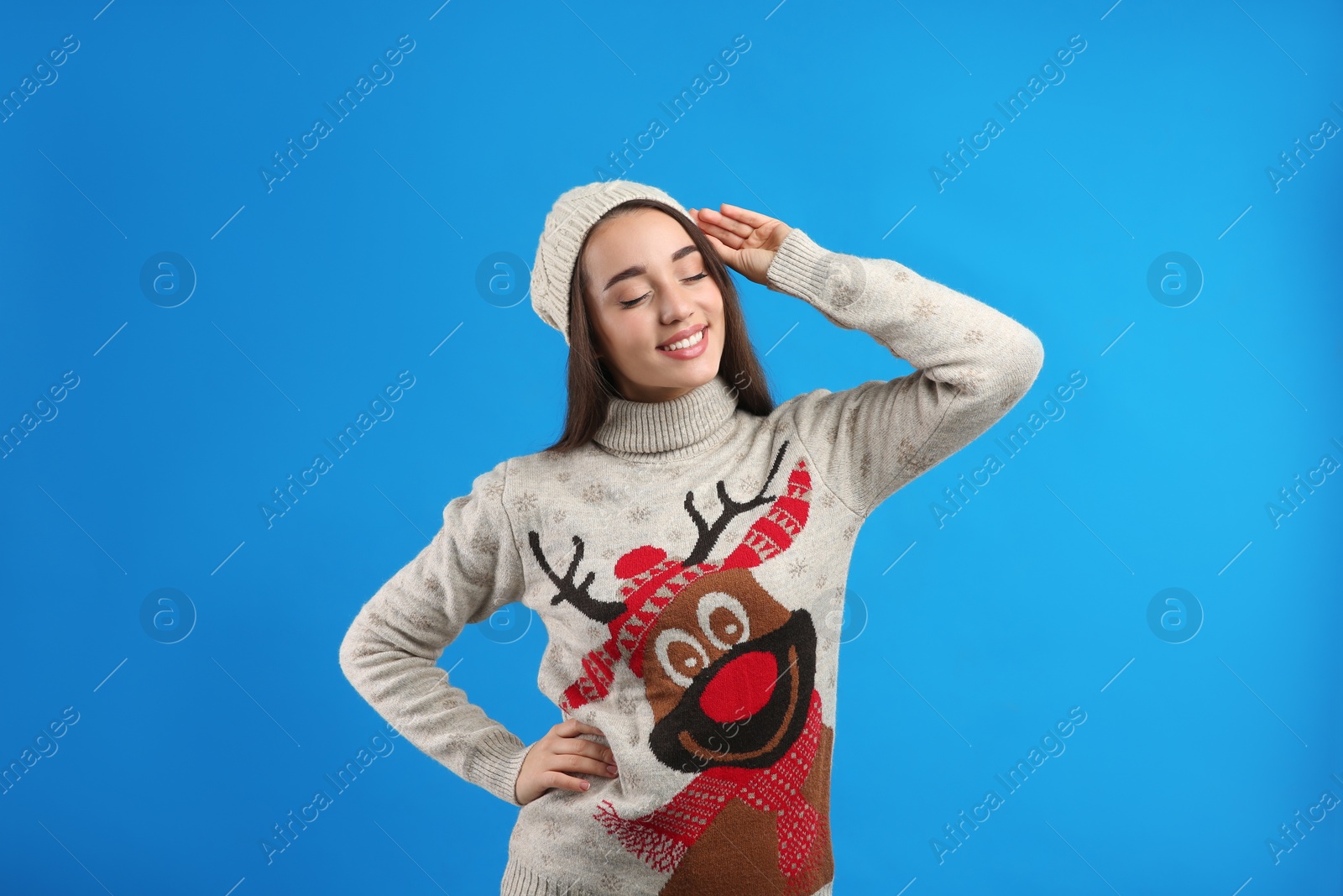 Photo of Young woman in Christmas sweater and hat on blue background
