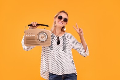 Photo of Portrait of happy hippie woman with retro radio receiver showing peace sign on yellow background