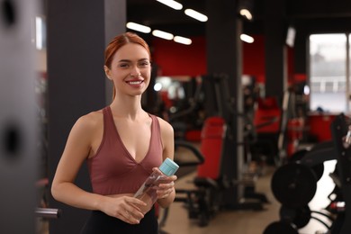 Beautiful young woman with bottle of water in gym, space for text