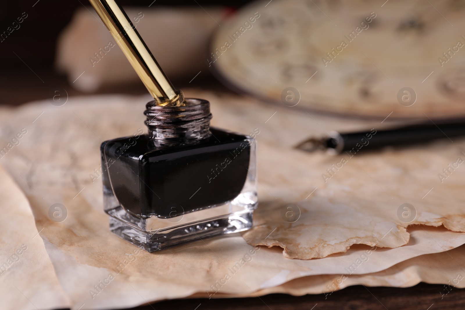 Photo of Inkwell with fountain pen and vintage parchment on table, closeup. Space for text