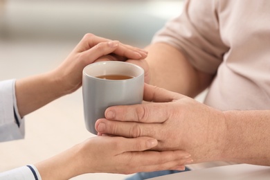 Photo of Nurse giving cup of tea to elderly man against blurred background, closeup. Assisting senior generation