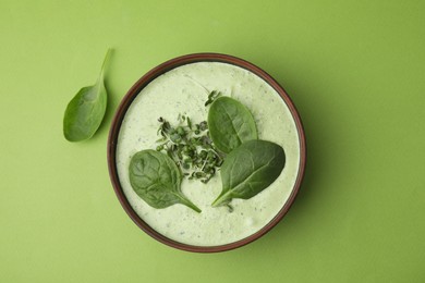 Delicious spinach cream soup with fresh leaves and microgreens in bowl on green background, top view