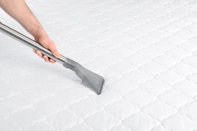 Photo of Man disinfecting mattress with vacuum cleaner, closeup. Space for text