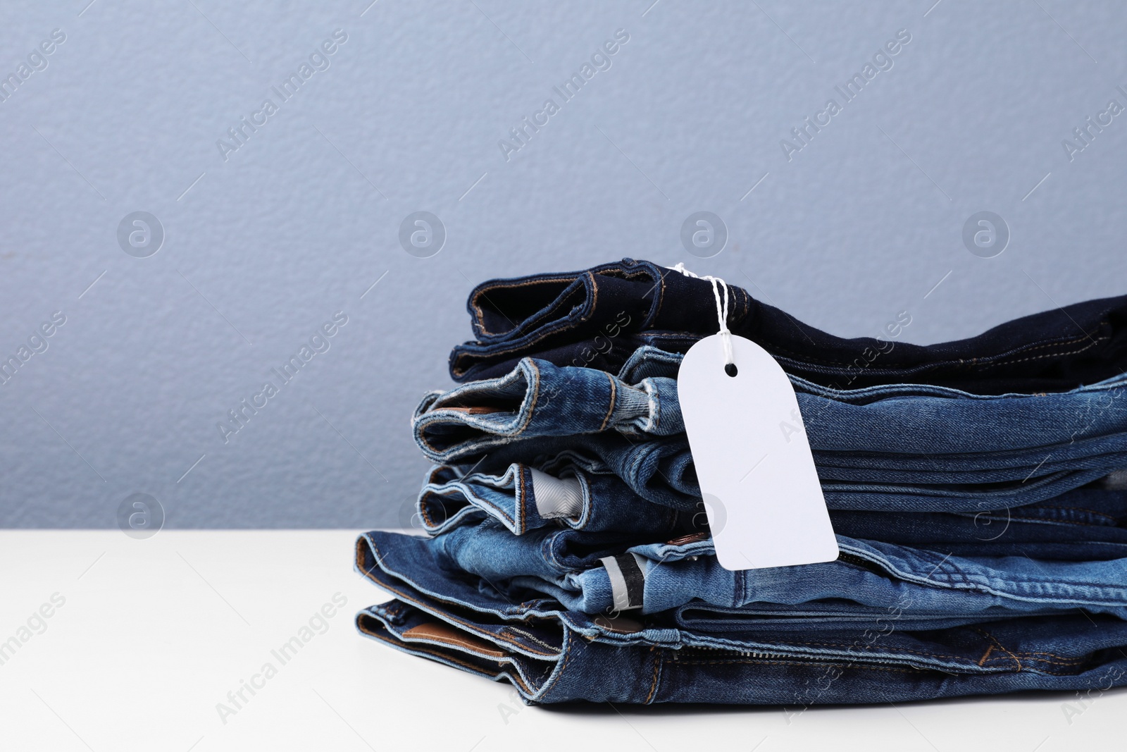 Photo of Stack of stylish jeans with tag on table