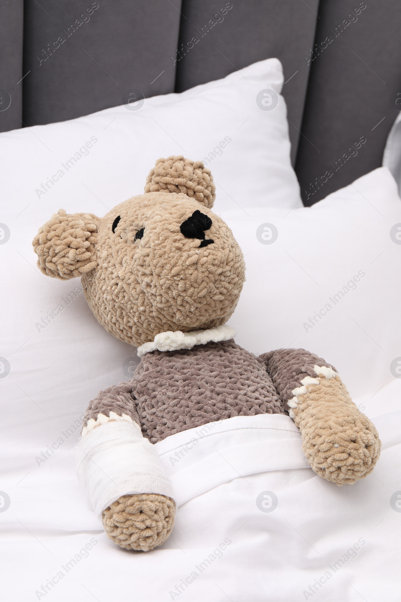 Photo of Toy cute bear with bandage under blanket in bed