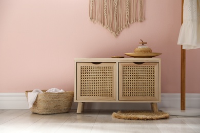 Photo of Wooden commode near pink wall in room. Interior design