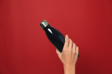 Woman holding modern dark thermos on red background, closeup