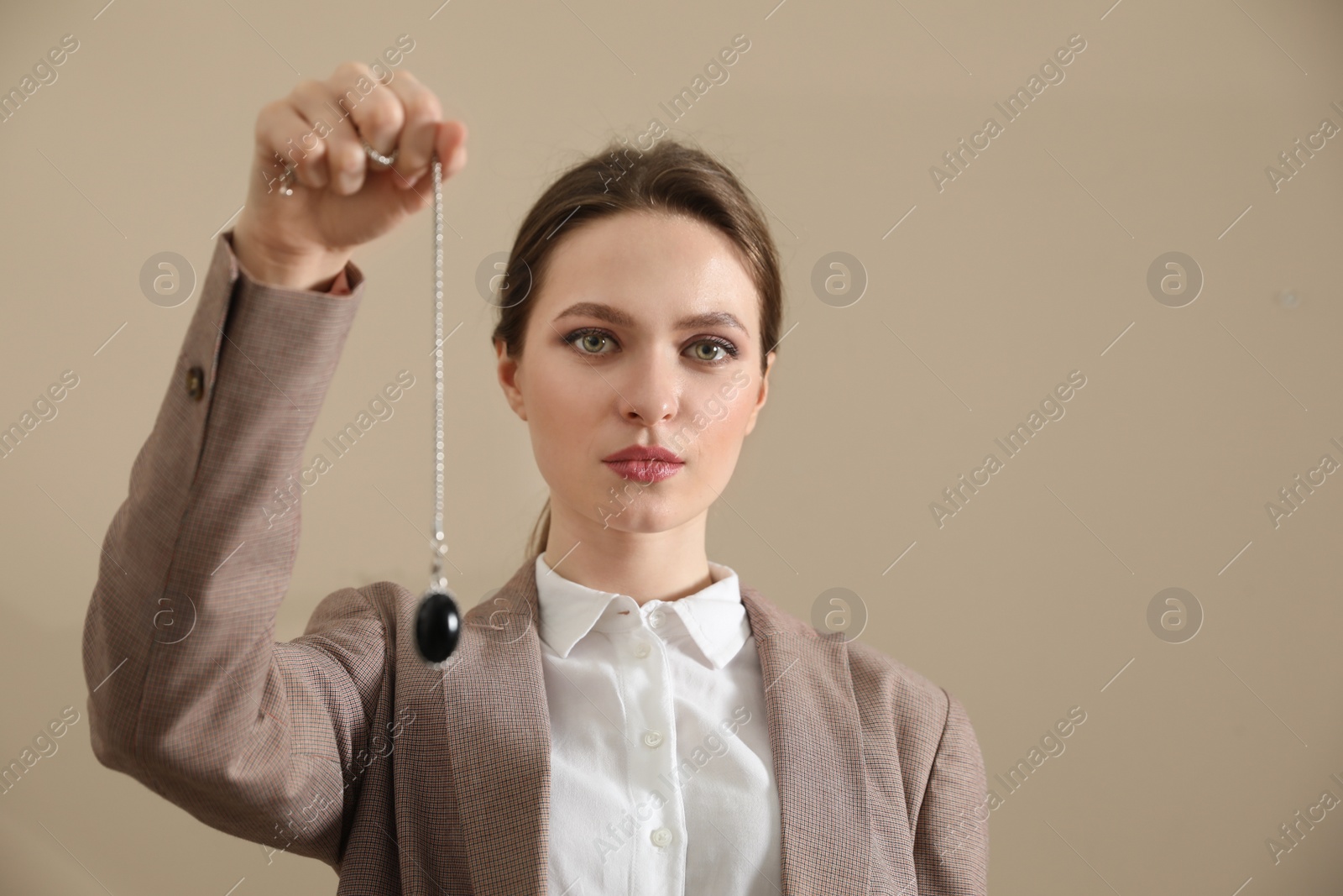 Photo of Psychotherapist with pendulum on beige background. Hypnotherapy session