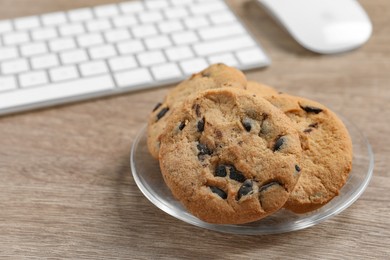 Photo of Chocolate chip cookies on wooden table at workplace, closeup