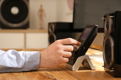 Man using remote to control audio speakers at table indoors, closeup