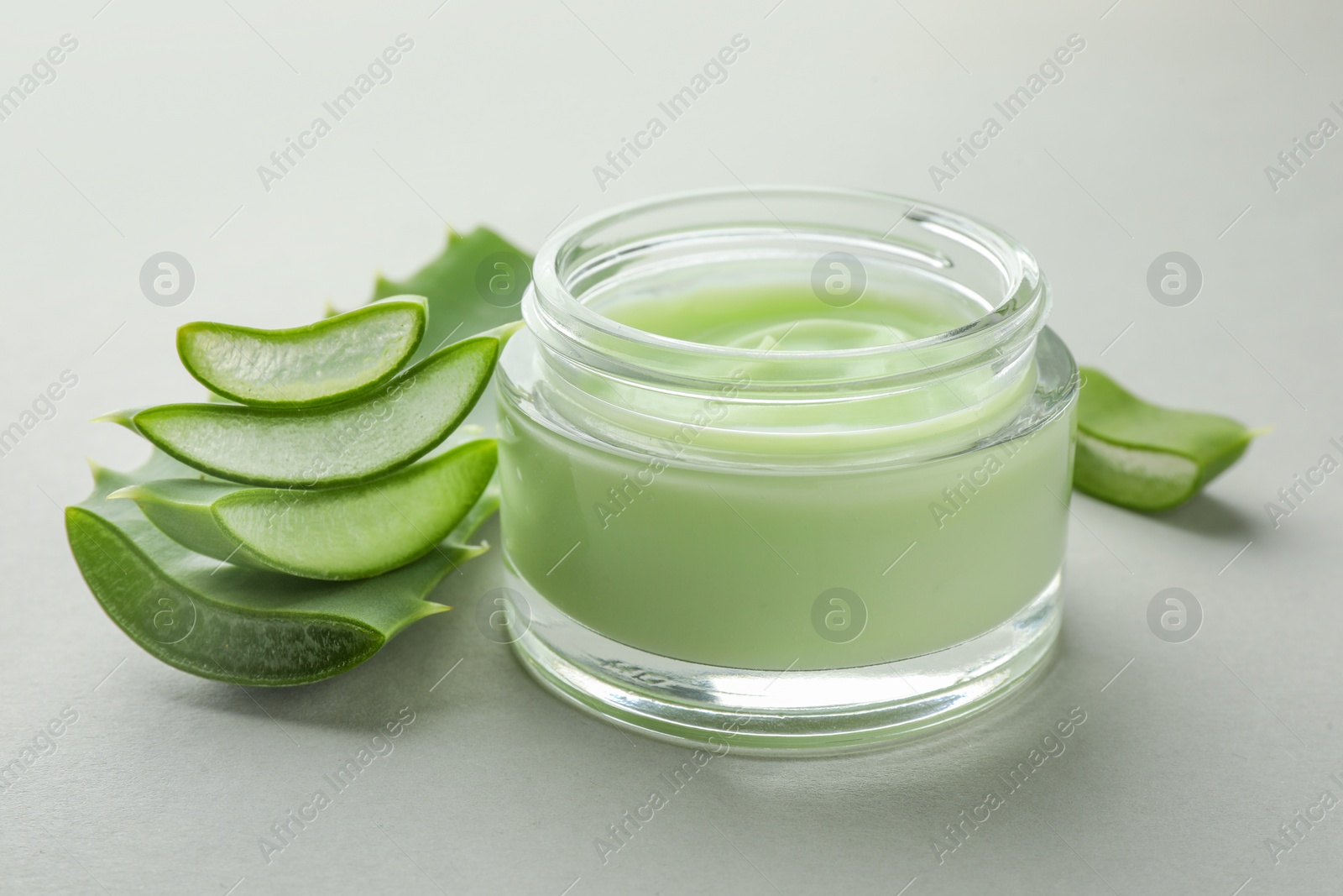 Photo of Jar with cream and cut aloe leaf on light grey background, closeup