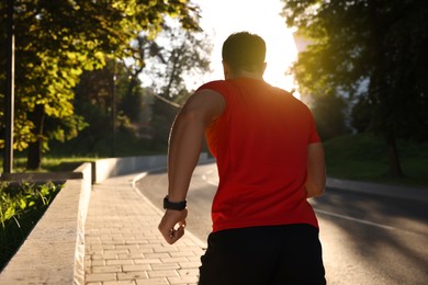 Man running outdoors on sunny day, back view. Space for text