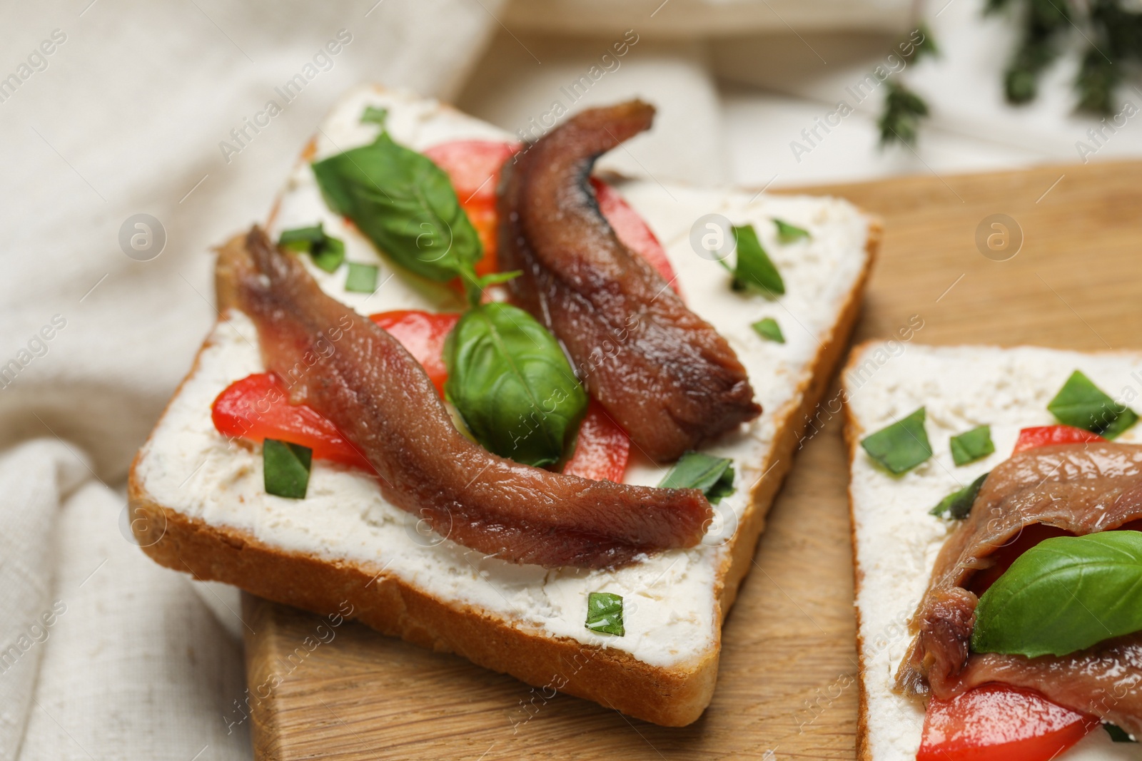 Photo of Delicious sandwiches with cream cheese, anchovies, tomatoes and basil on wooden board, closeup