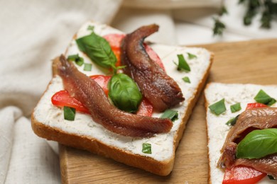 Photo of Delicious sandwiches with cream cheese, anchovies, tomatoes and basil on wooden board, closeup