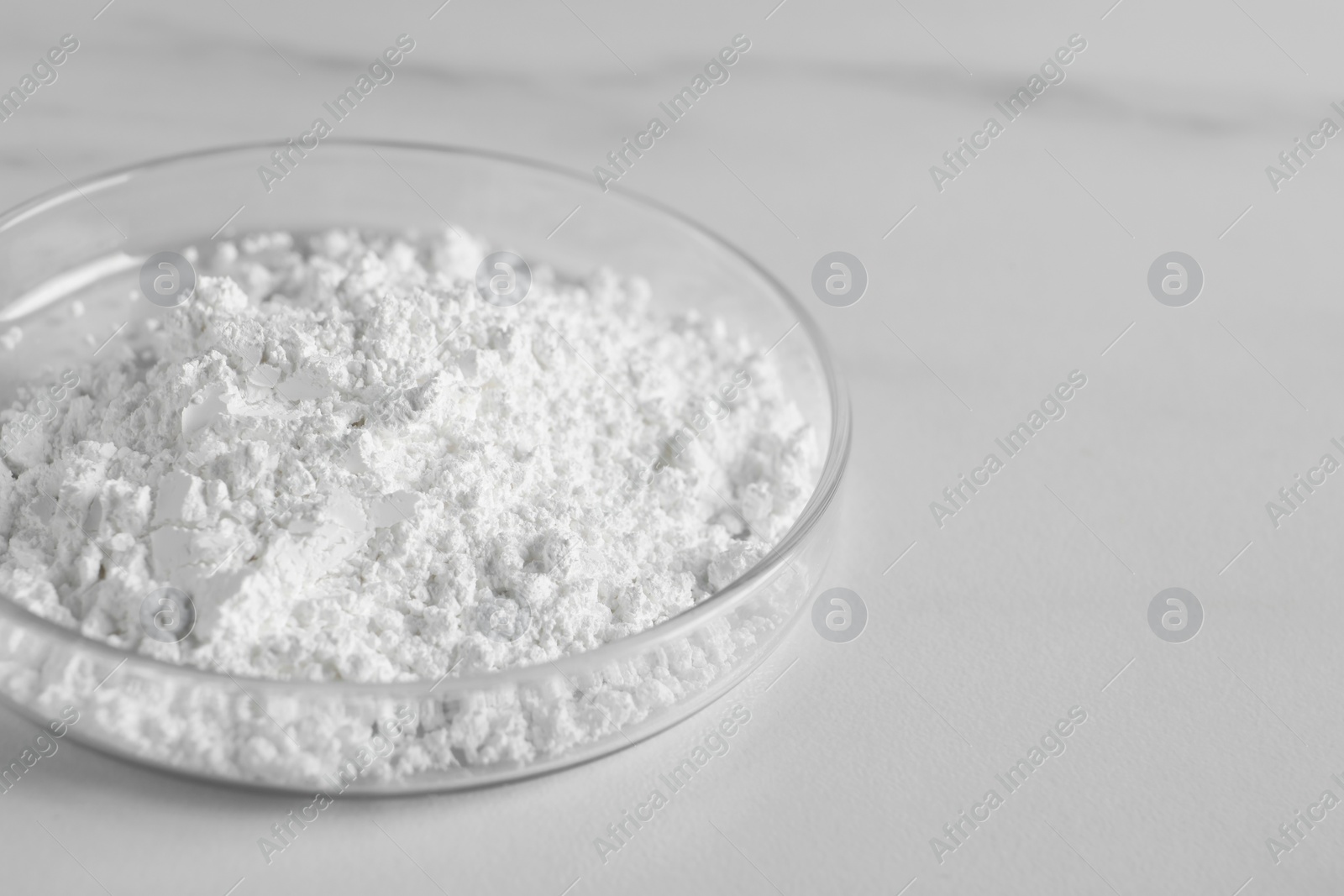 Photo of Petri dish with calcium carbonate powder on white marble table, closeup. Space for text