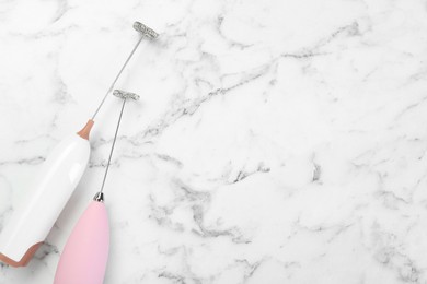 Pink milk frother wands on white marble table, top view. Space for text