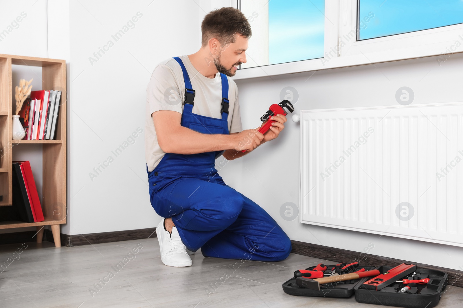 Photo of Professional plumber using adjustable wrench for installing new heating radiator in room